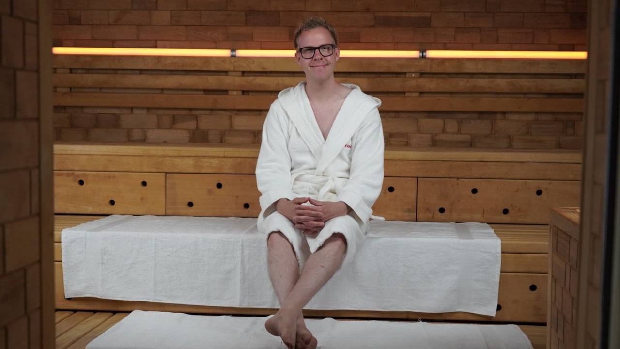 Ein Mann im weißen Bademantel sitzt auf der Holzstufe einer Sauna