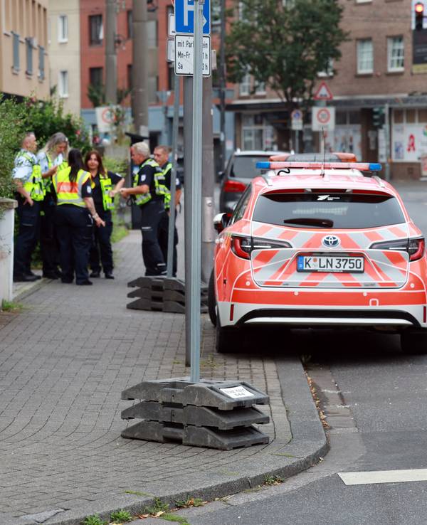 Eine Frau mit Rollkoffer geht vor einem Einsatzwagen über die Straße