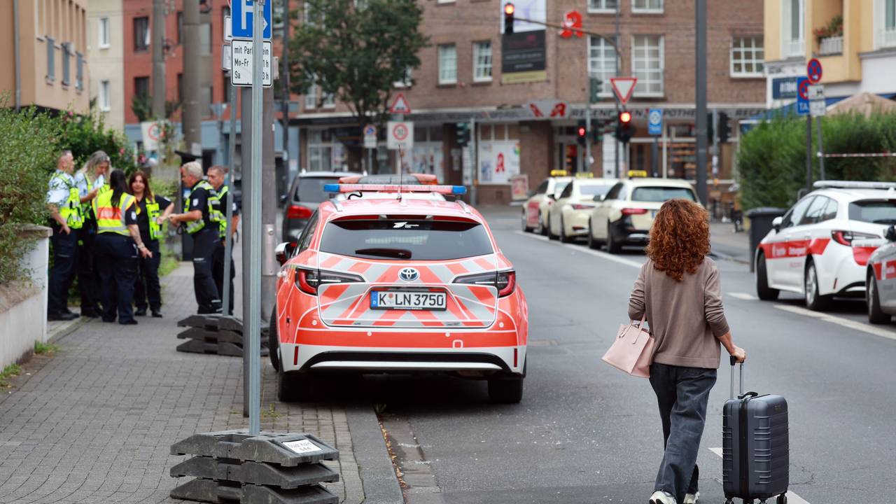 Eine Frau mit Rollkoffer geht vor einem Einsatzwagen über die Straße