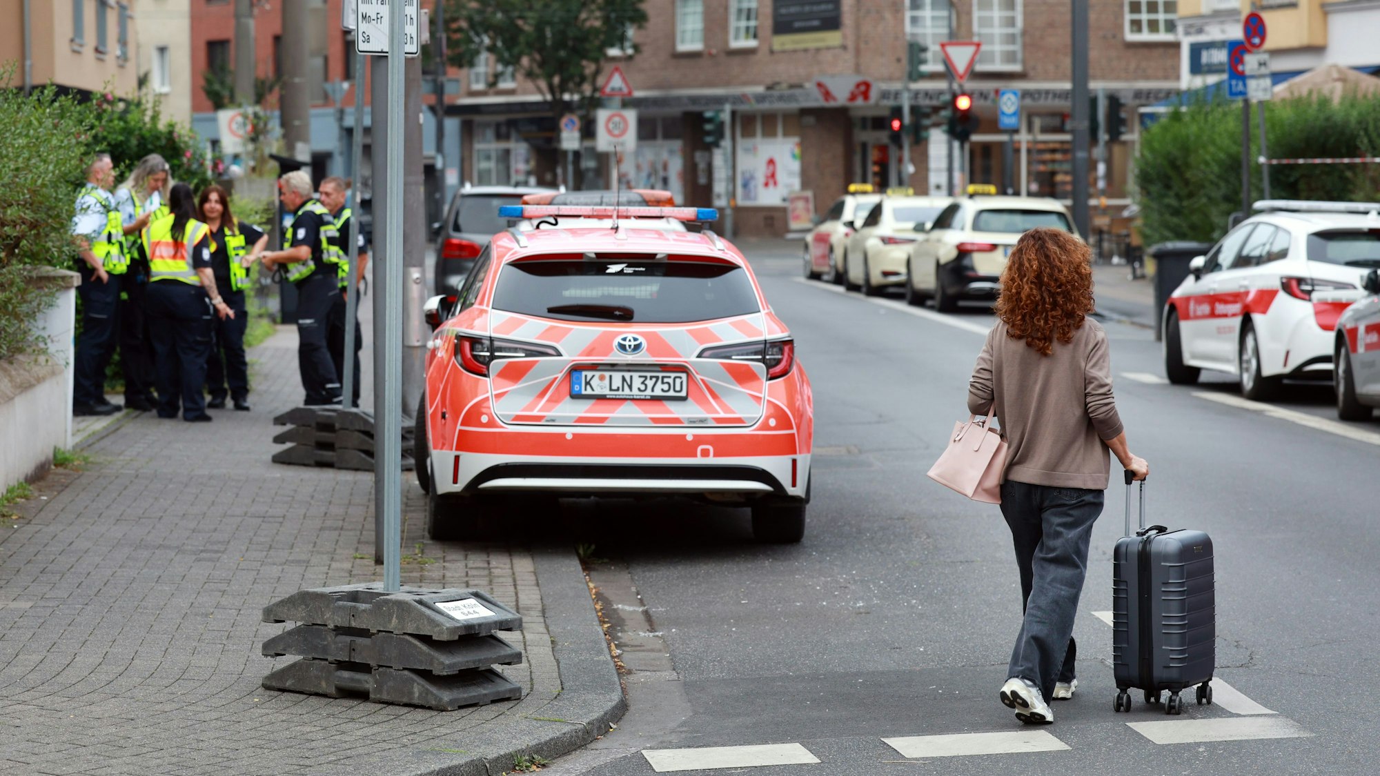 Eine Frau mit Rollkoffer geht vor einem Einsatzwagen über die Straße