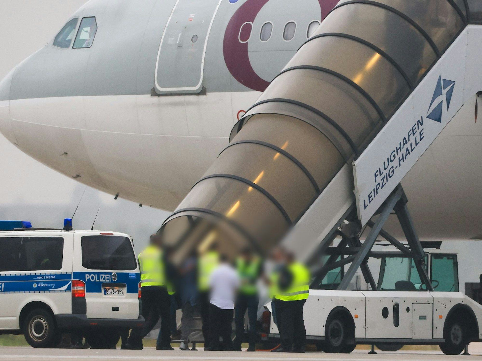 Menschen besteigen ein Flugzeug der Qatar Airways, vor dem Fahrzeuge der Bundespolizei stehen auf dem Vorfeld am Flughafen Leipzig/Halle.