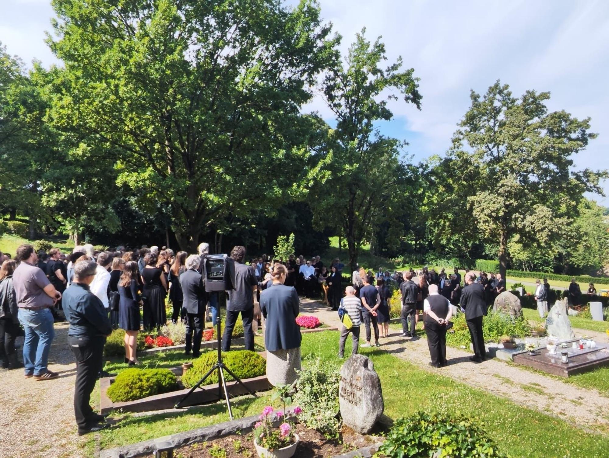 Menschen stehen auf einem Friedhof an einem Grab.