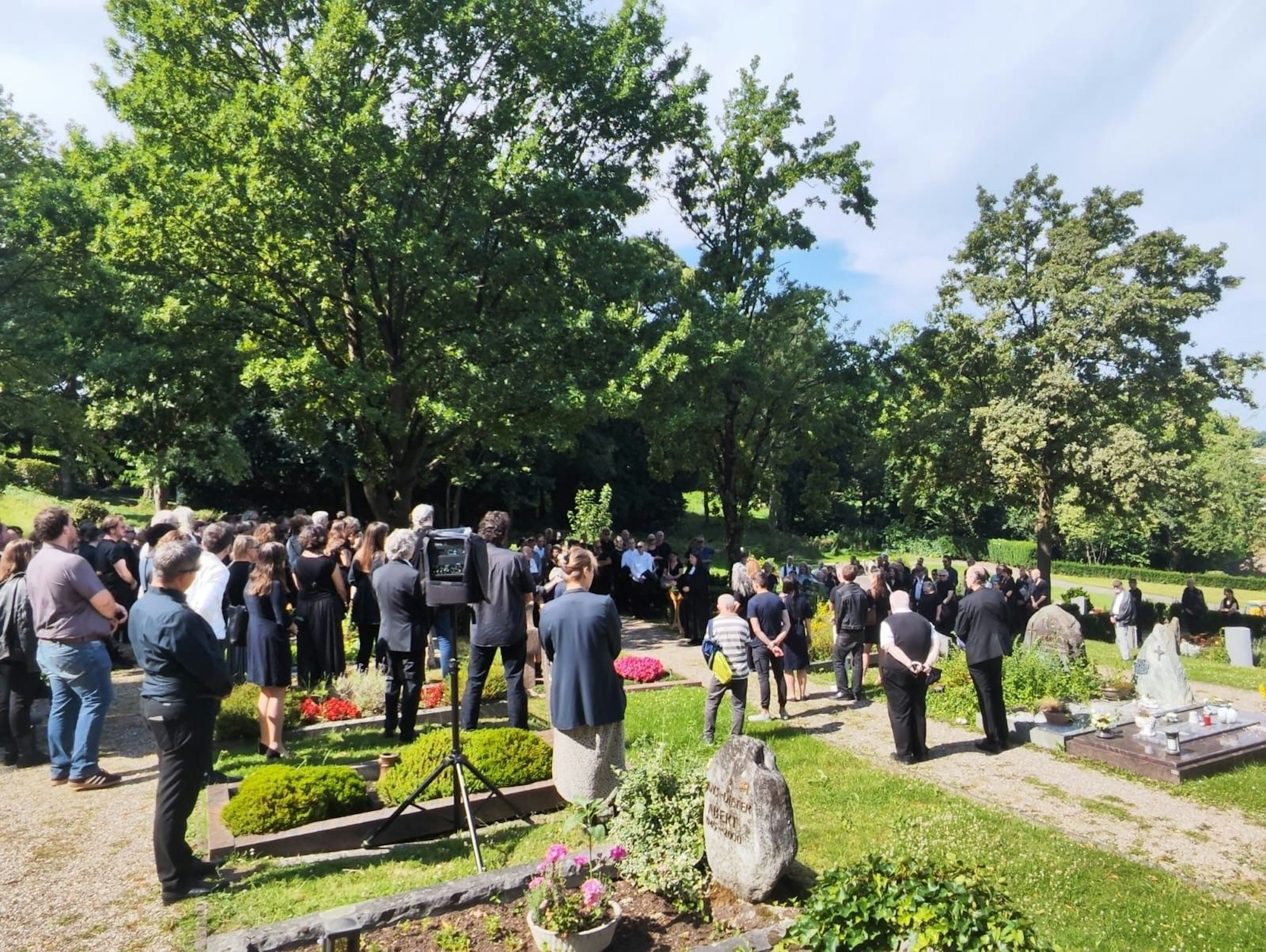 Menschen stehen auf einem Friedhof an einem Grab.