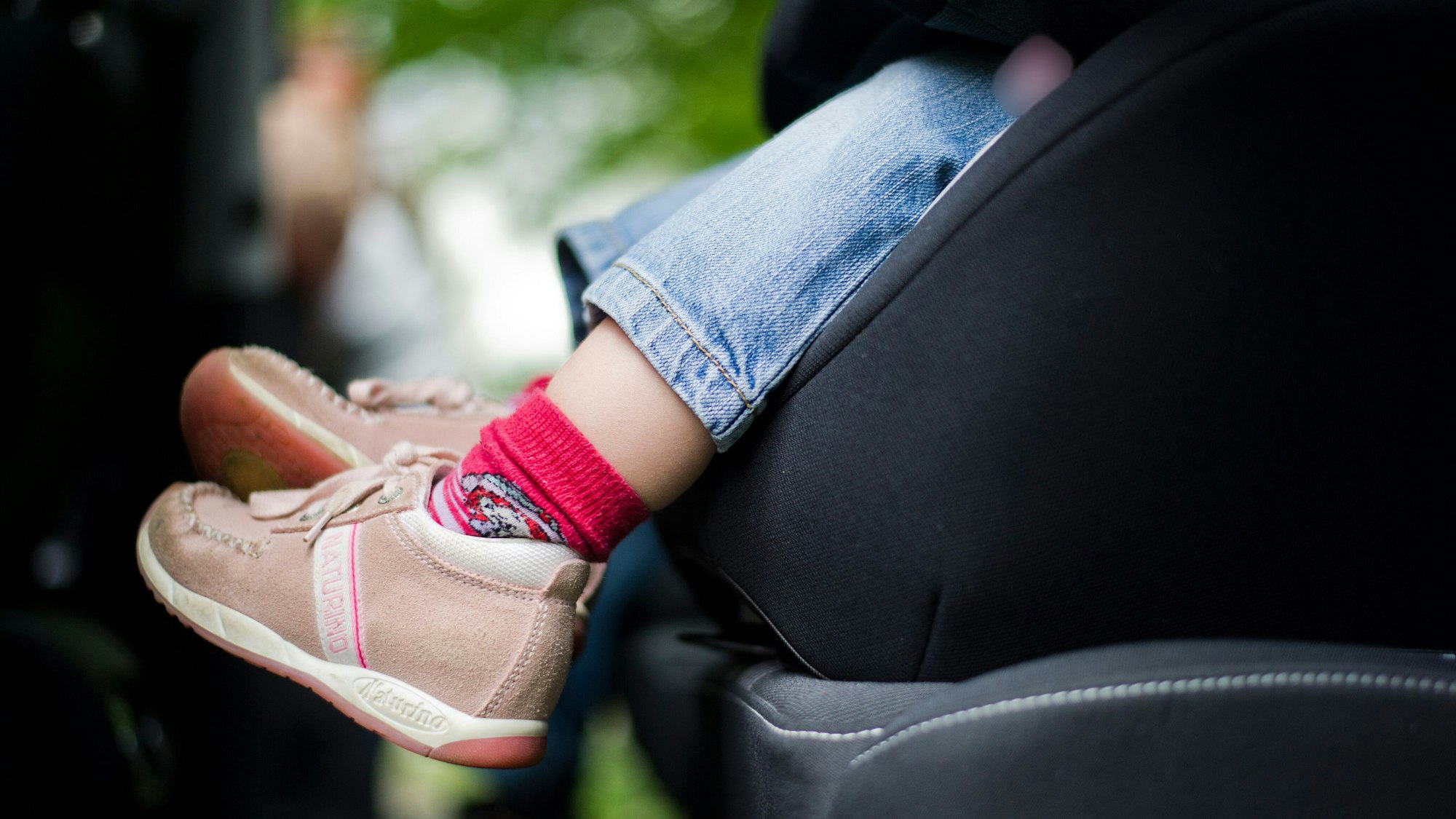 Die Beine eines Kindes, das in einem Autositz sitzt.