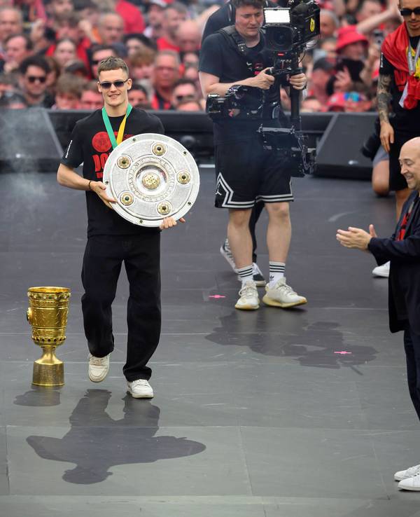 Florian Wirtz geht mit der Meisterschale über eine Bühne in der BayArena, Fernando Carro applaudiert.
