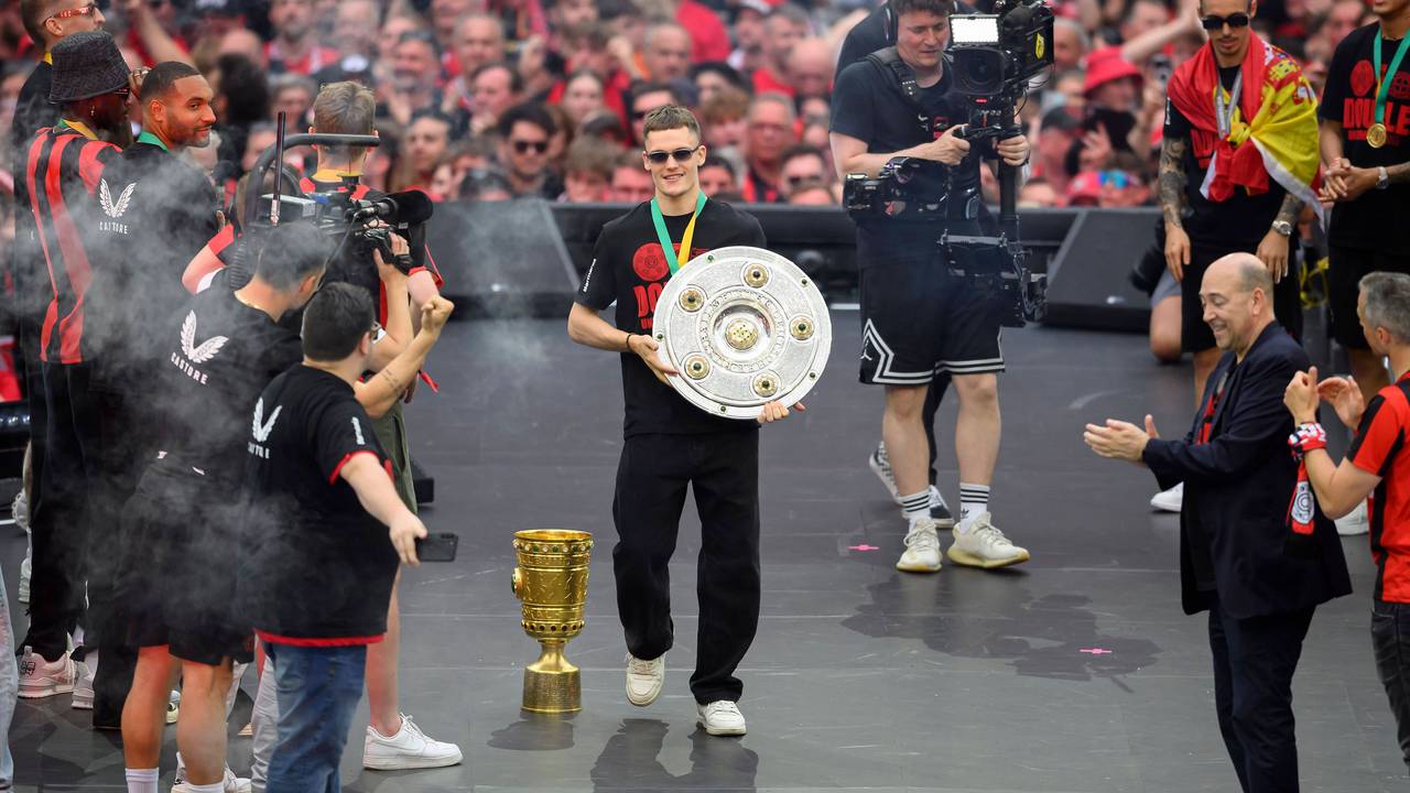 Florian Wirtz geht mit der Meisterschale über eine Bühne in der BayArena, Fernando Carro applaudiert.