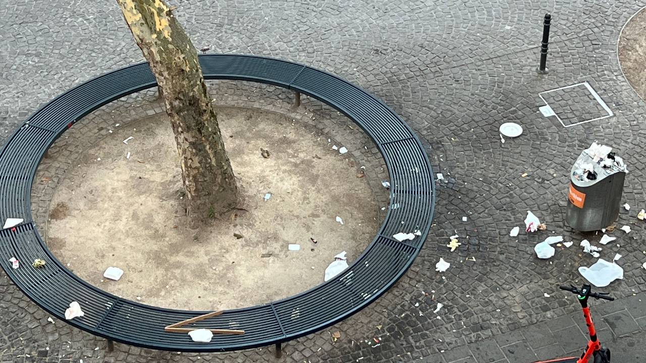 Auf einer runden Sitzbank liegt Müll, ebenso auf dem Boden rund um einen Mülleimer.
