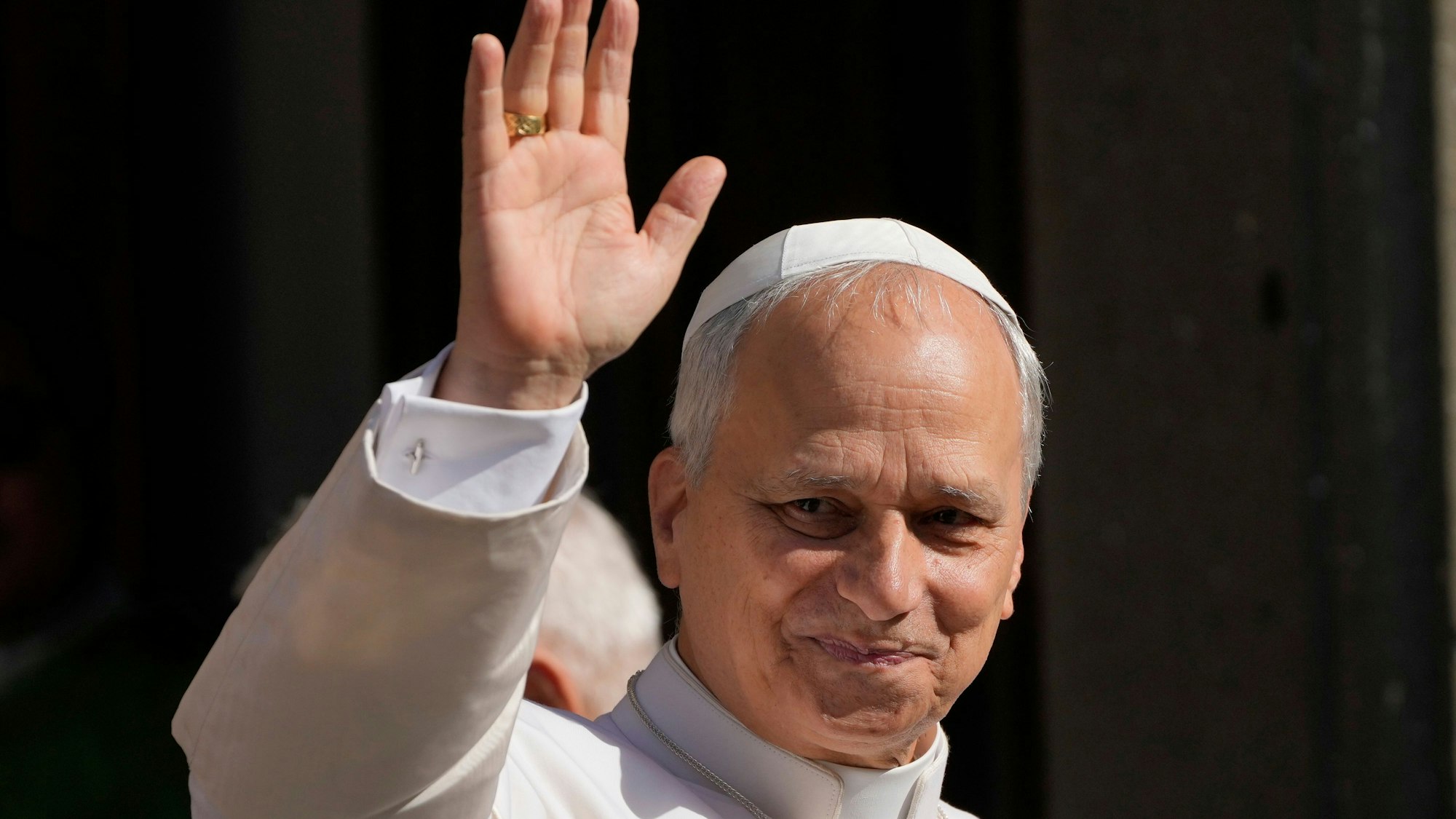 Papst Leo XIV. winkt und schmunzelt dabei.