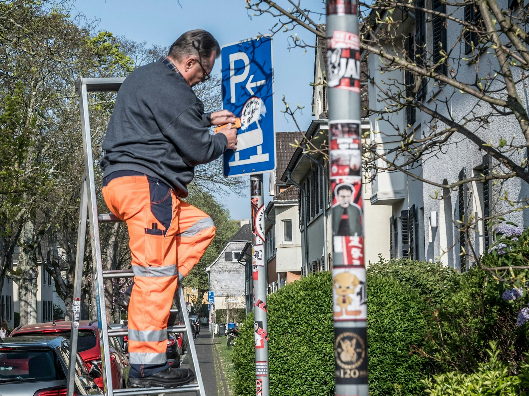 Ein Mitarbeiter der Technischen Betriebe Leverkusen (TBL) entfernt mühsam Aufkleber von einem Verkehrsschild.