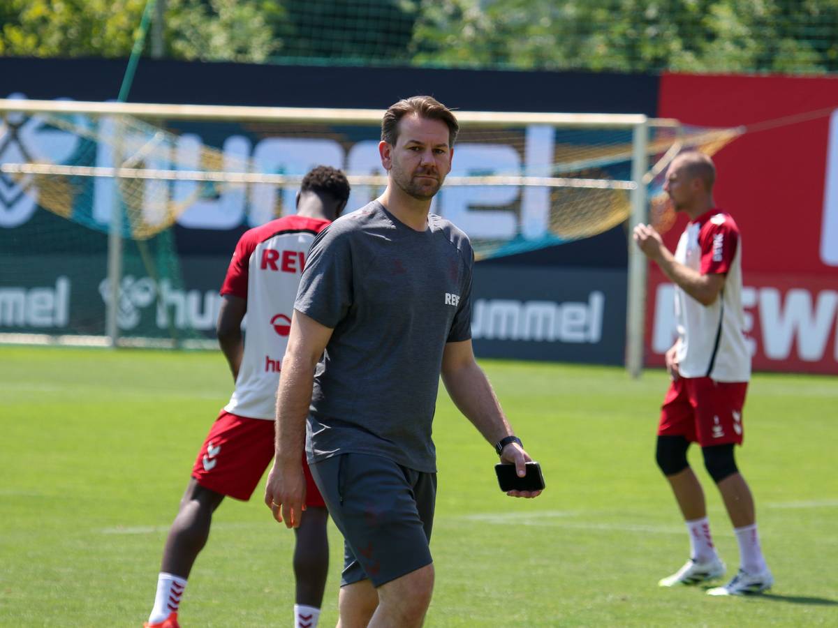 Thomas Kessler geht mit dem Handy in der Hand beim Training des 1. FC Köln über den Platz.