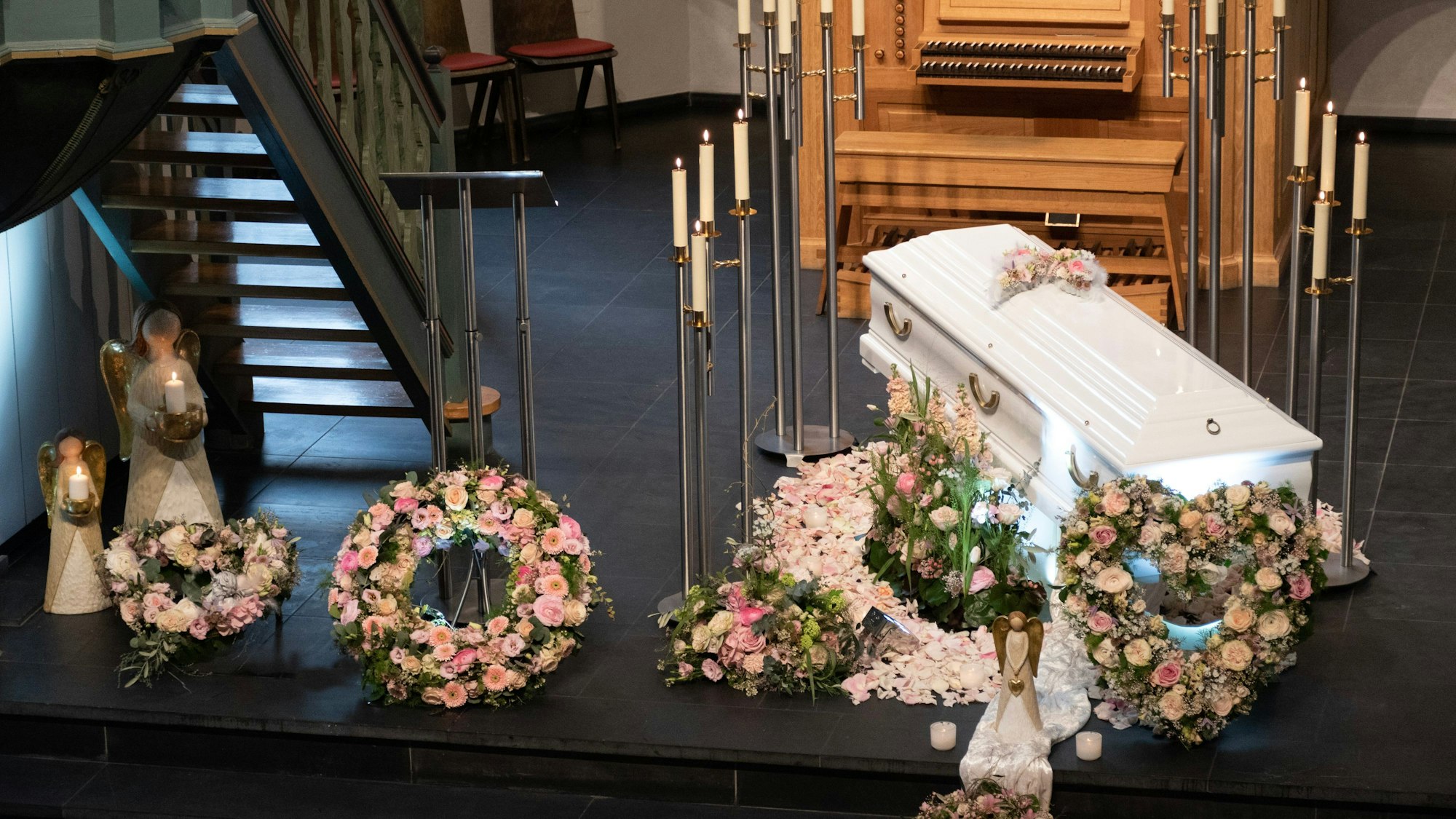 Ein Sarg steht in einer Kirche, um ihn herum liegen Blumenkränze.