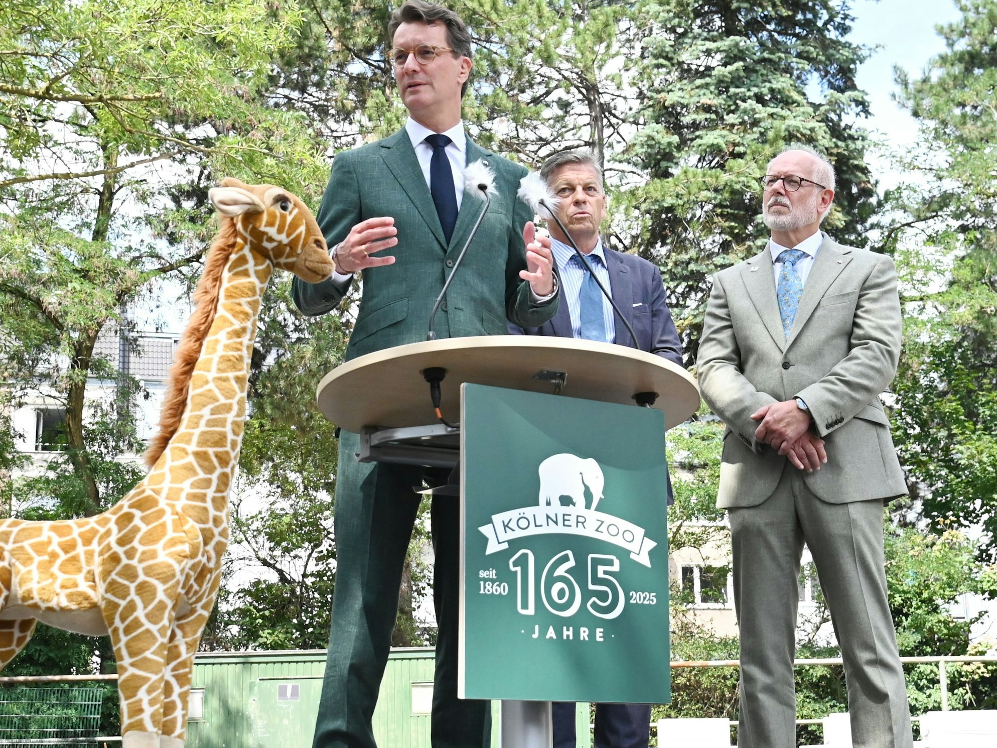 Drei Männer stehen neben einer Plüschtier-Giraffe.