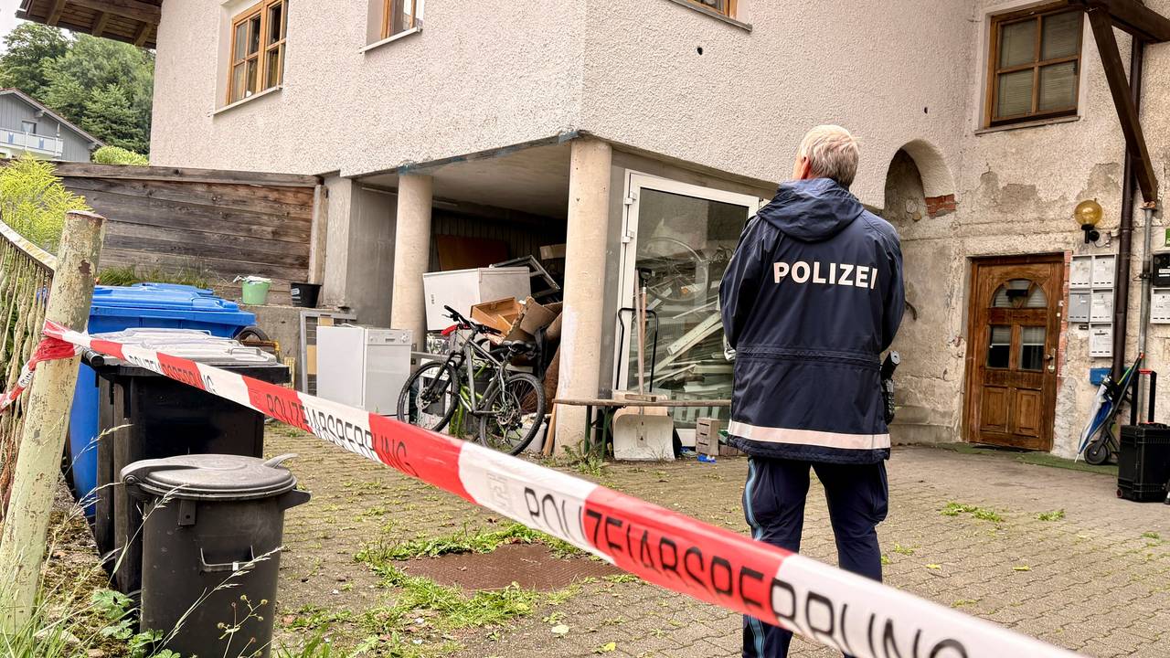 Ein Polizist steht hinter einer Absperrung vor einem Mehrfamilienhaus. In dem Haus im niederbayerischen Zwiesel sind drei Leichen gefunden worden. Man gehe derzeit von einem Tötungsdelikt aus, sagte eine Polizeisprecherin. Ein Verdächtiger sei in Österreich festgenommen worden.