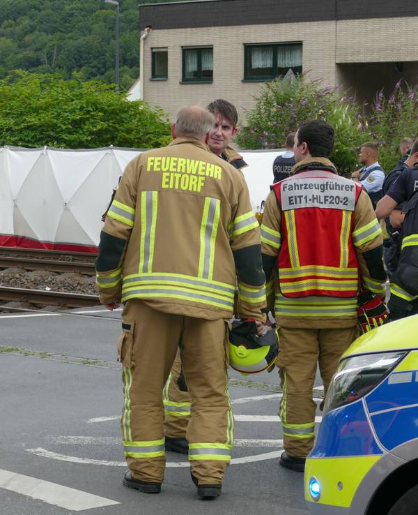 Einsatzkräfte von Polizei und Feuerwehr stehen an einer Unfallstelle an einem Bahnübergang in Eitorf. Zwei Menschen sind dort von einer S-Bahn erfasst und tödlich verletzt worden.