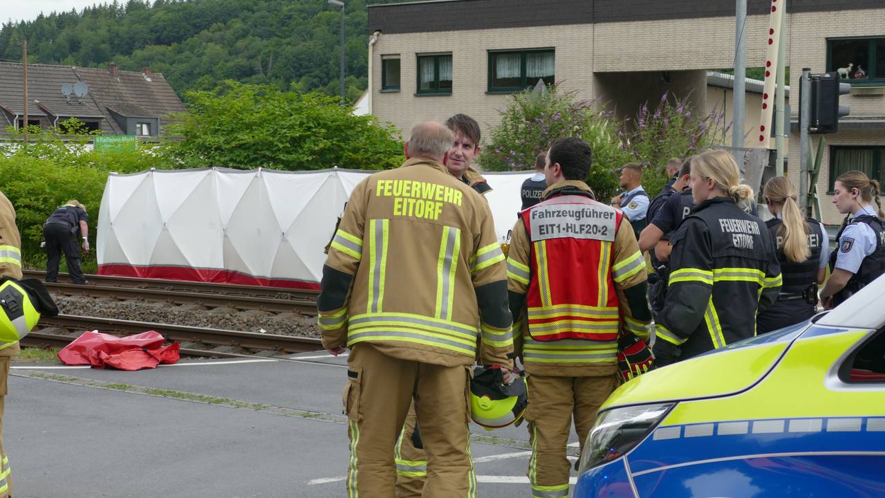 Einsatzkräfte von Polizei und Feuerwehr stehen an einer Unfallstelle an einem Bahnübergang in Eitorf. Zwei Menschen sind dort von einer S-Bahn erfasst und tödlich verletzt worden.