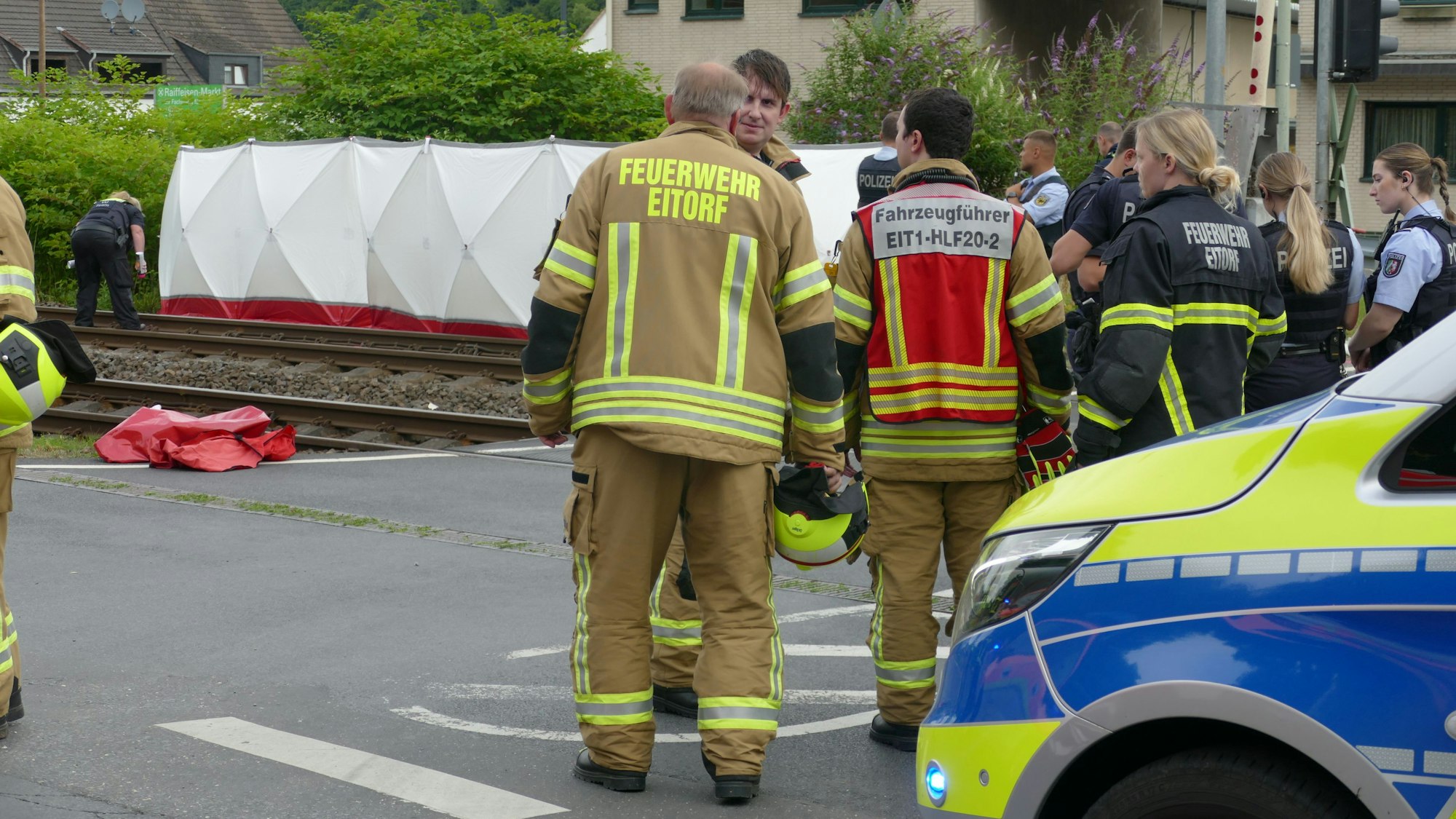 Einsatzkräfte von Polizei und Feuerwehr stehen an einer Unfallstelle an einem Bahnübergang in Eitorf. Zwei Menschen sind dort von einer S-Bahn erfasst und tödlich verletzt worden.