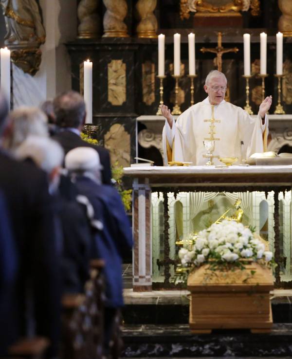 Ein Pfarrer steht in einer mit Menschen gefüllten Kirche hinter dem Altar, davor steht ein Sarg mit Blumen.
