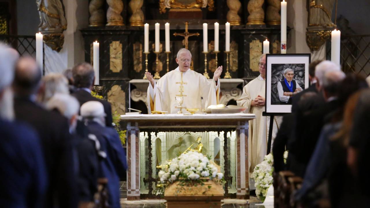 Ein Pfarrer steht in einer mit Menschen gefüllten Kirche hinter dem Altar, davor steht ein Sarg mit Blumen.