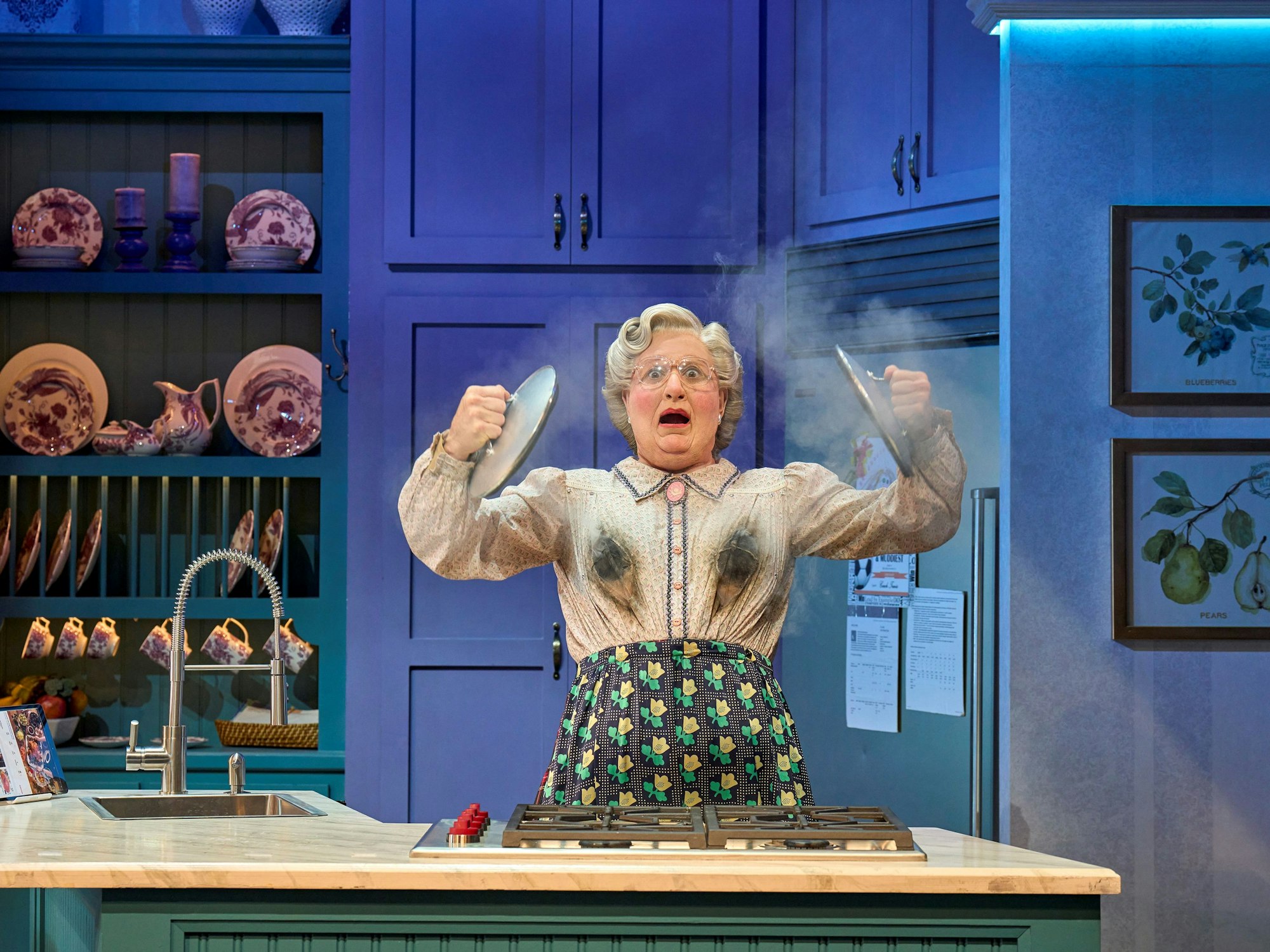 Mrs. Doubtfire steht in einer Küche mit Ruß auf der Kleidung und dampfenden Töpfen, sichtlich überrascht.