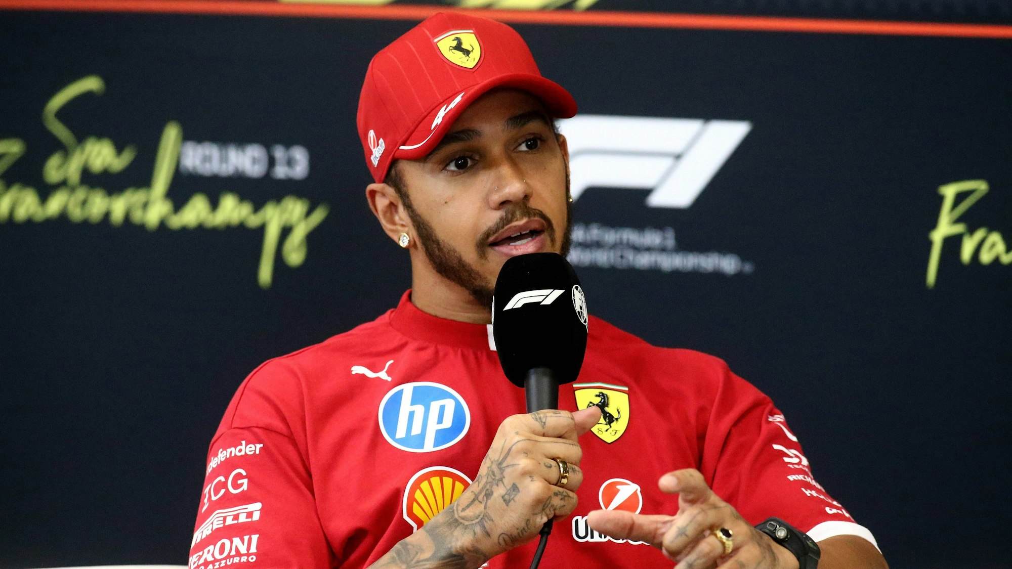Lewis Hamilton spricht bei einer Pressekonferenz im Ferrari-Outfit.