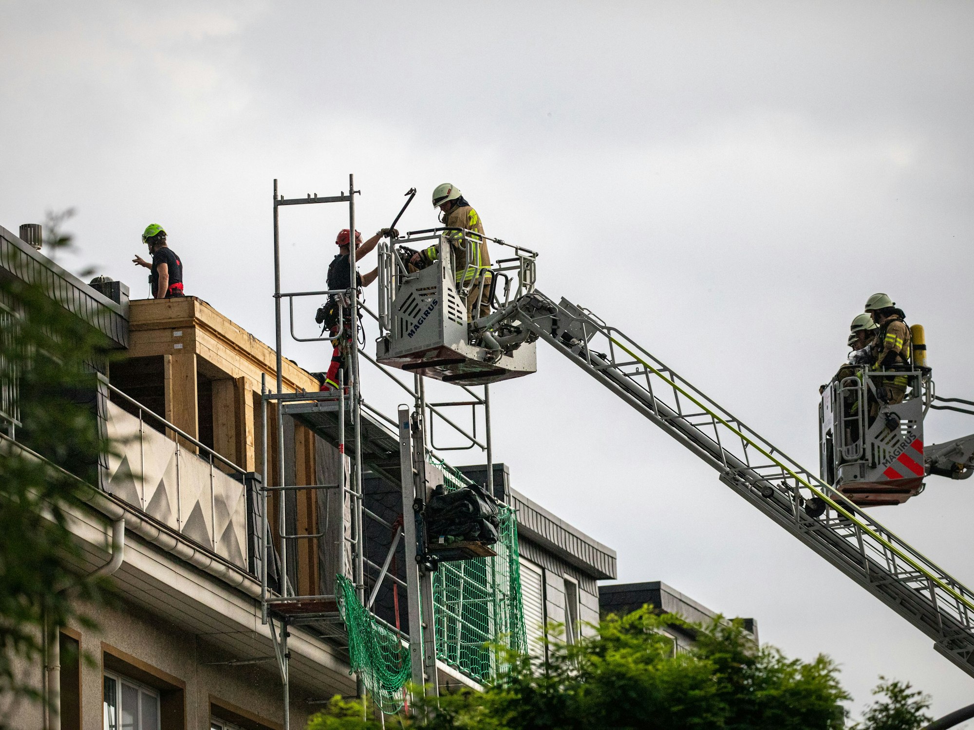 Zwei Drehleitern, in denen sich Feuerwehrleute befinden, reichen an ein Hausdach.
