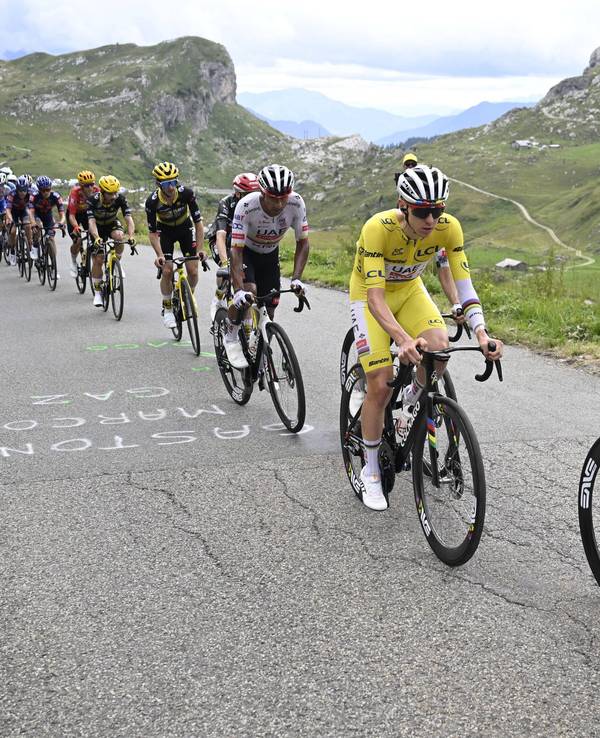 Eine Gruppe von Tour-Fahrern mit Tadej Pogacar im Gelben Trikot in den Alpen.
