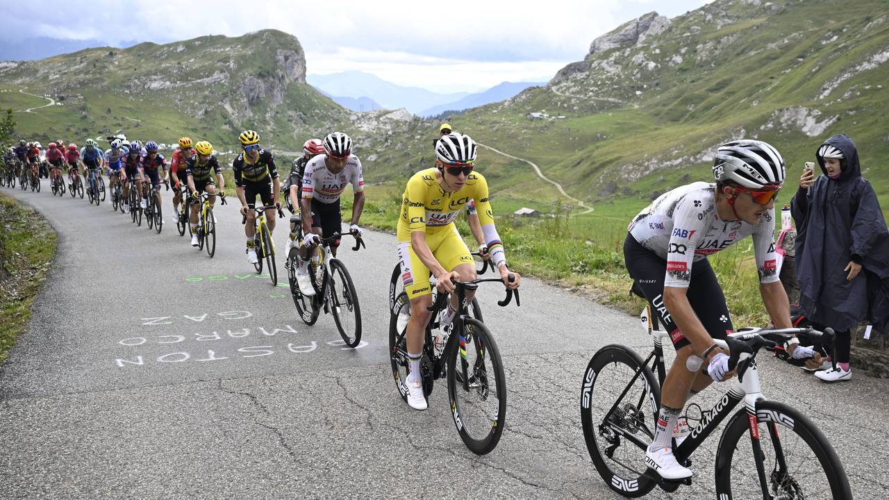 Eine Gruppe von Tour-Fahrern mit Tadej Pogacar im Gelben Trikot in den Alpen.