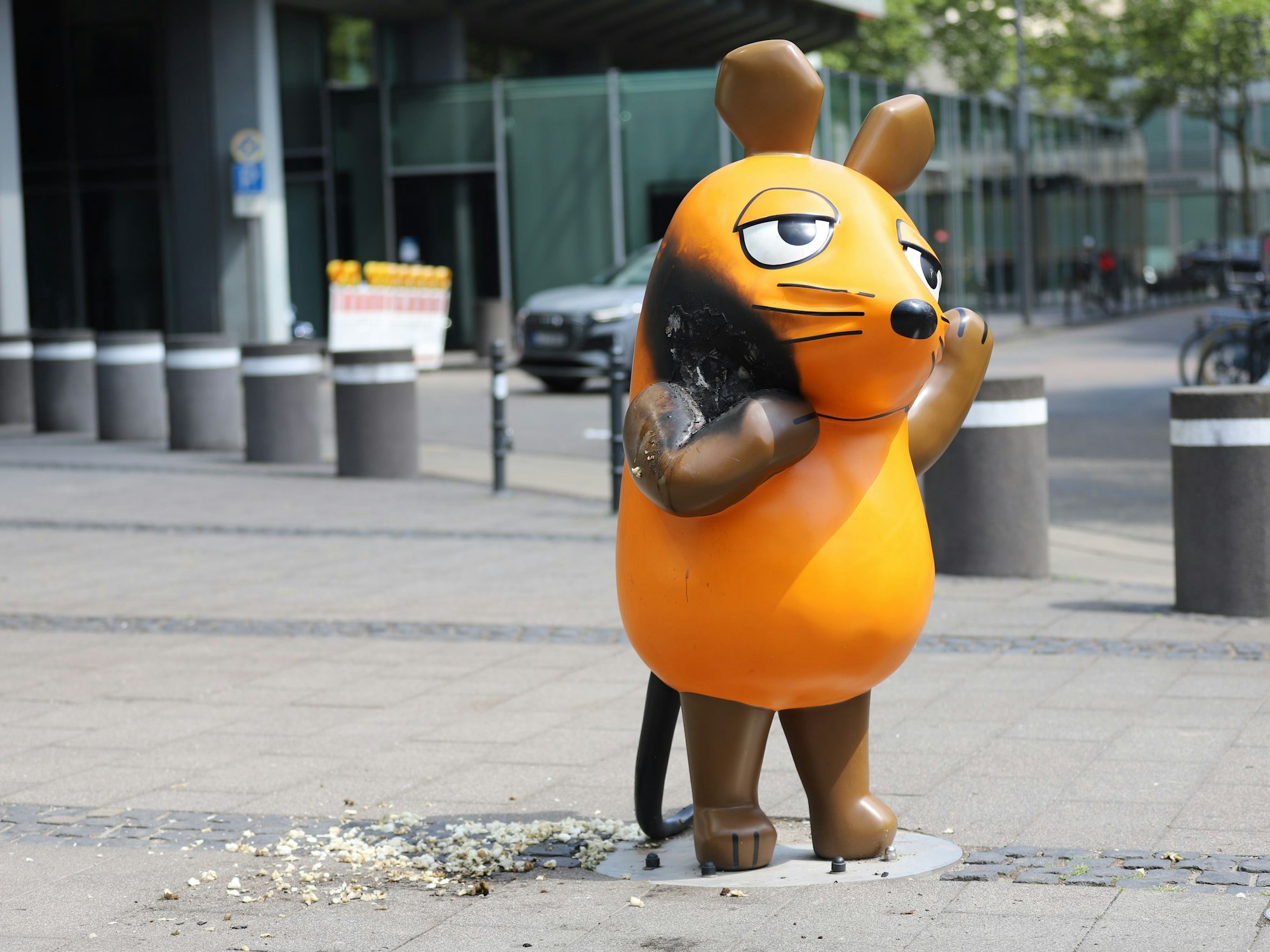 Mit einem großen Brandfleck steht die Maus vor dem WDR-Gebäude.