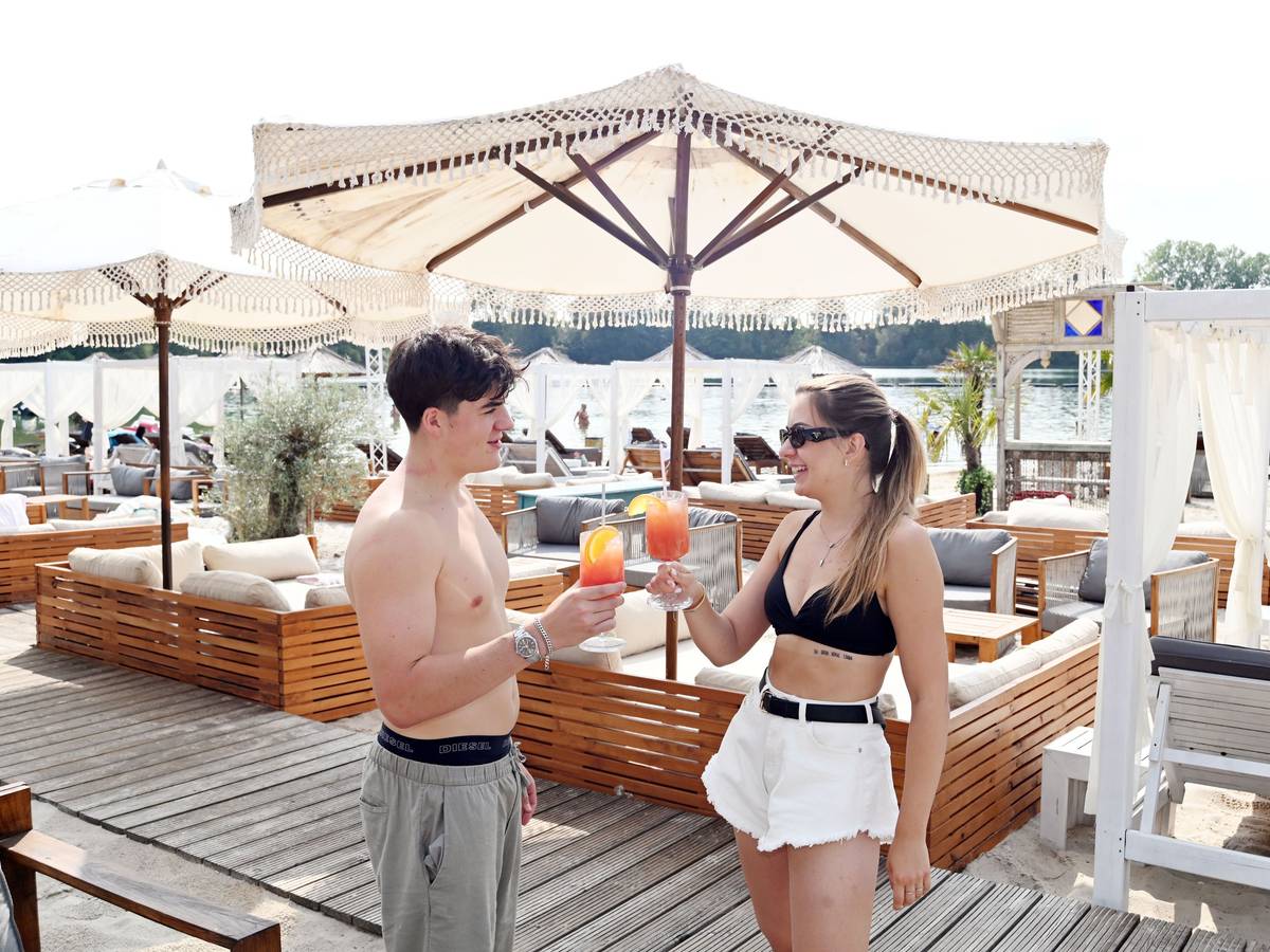 In einem Beachclub prosten sich eine Frau und ein Mann mit einem Cocktail zu.