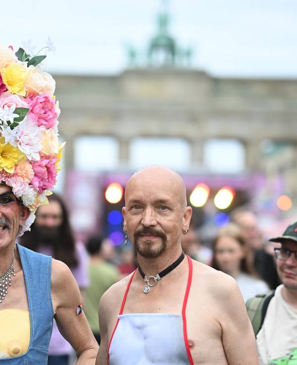 Ein Mann trägt einen Hut aus Blumen, neben ihm ein Mann mit einer Schürze.