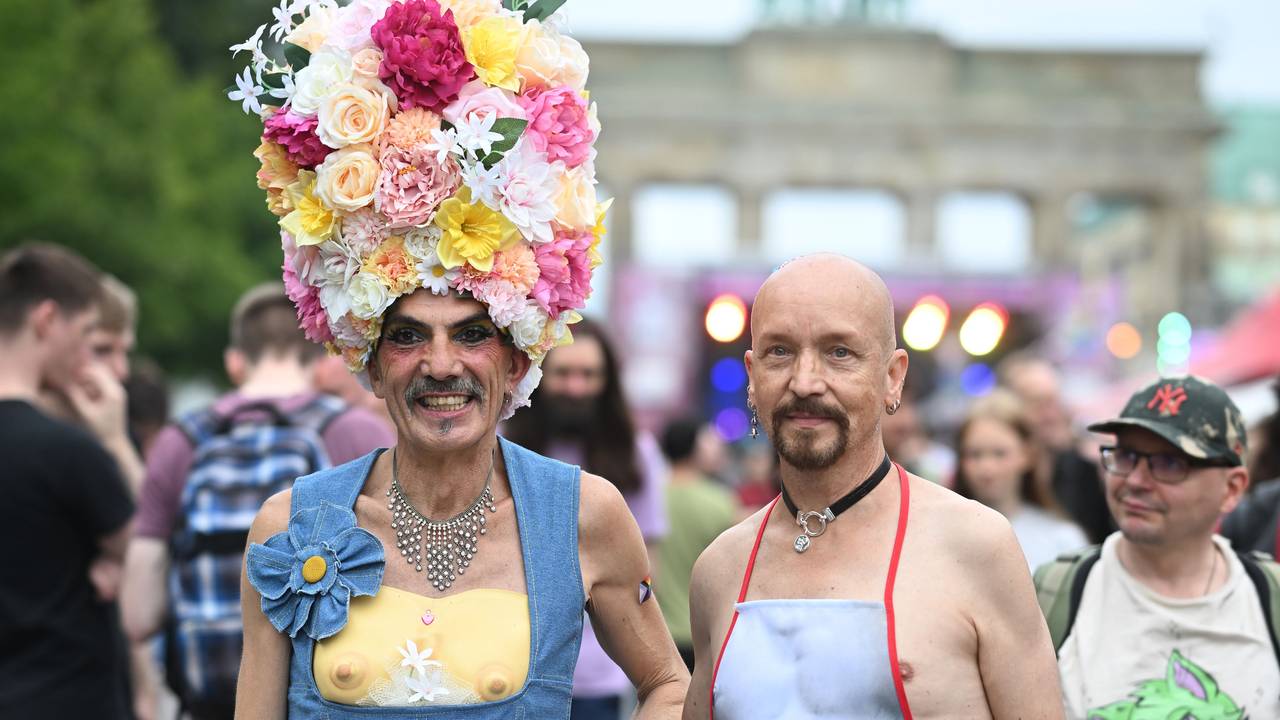 Ein Mann trägt einen Hut aus Blumen, neben ihm ein Mann mit einer Schürze.