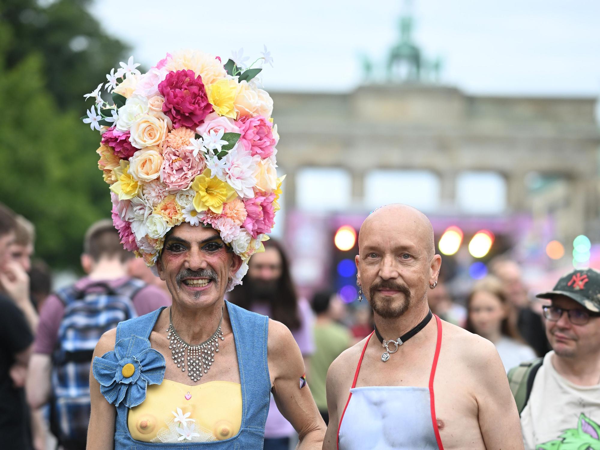 Ein Mann trägt einen Hut aus Blumen, neben ihm ein Mann mit einer Schürze.