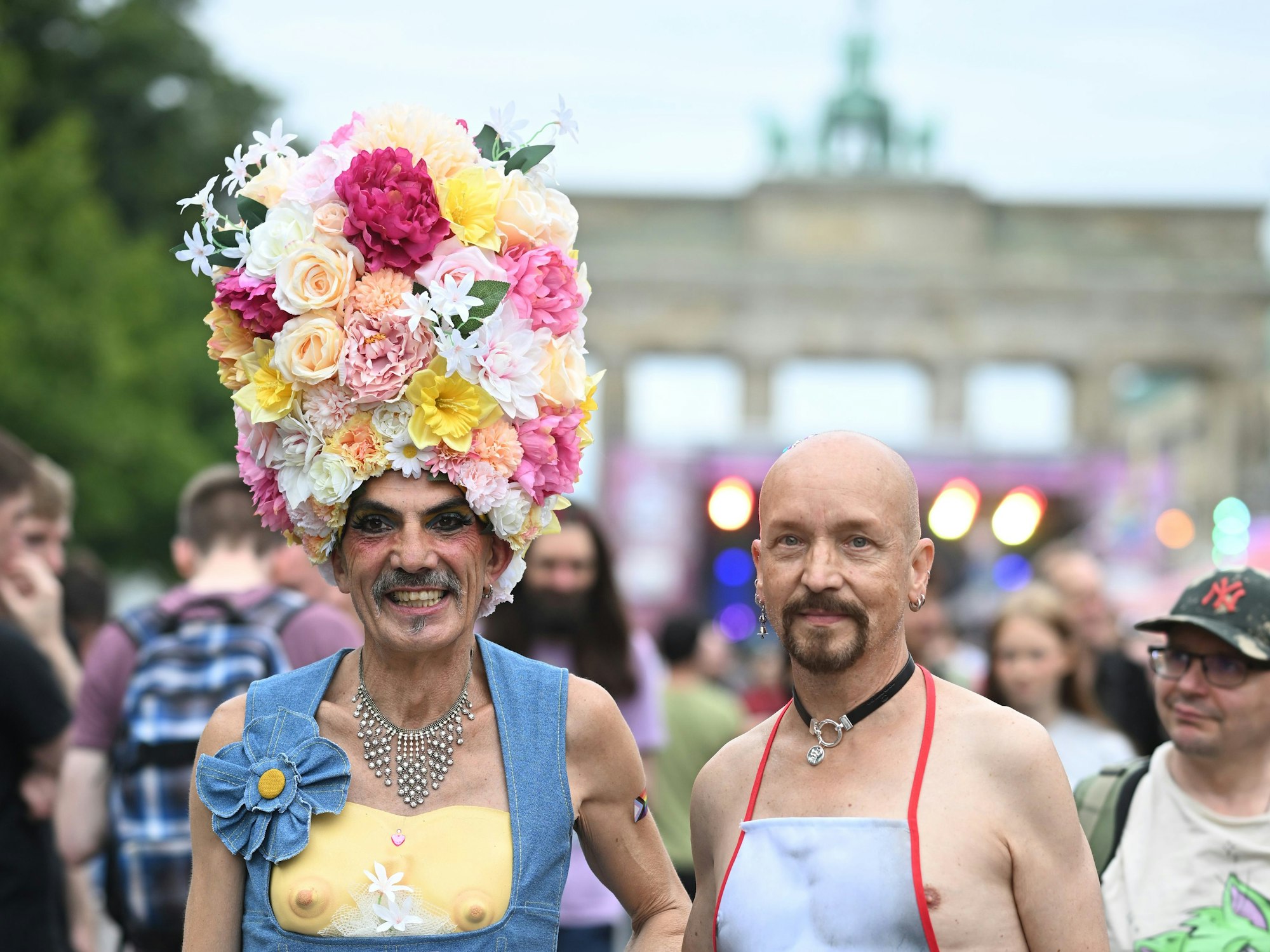 Ein Mann trägt einen Hut aus Blumen, neben ihm ein Mann mit einer Schürze.
