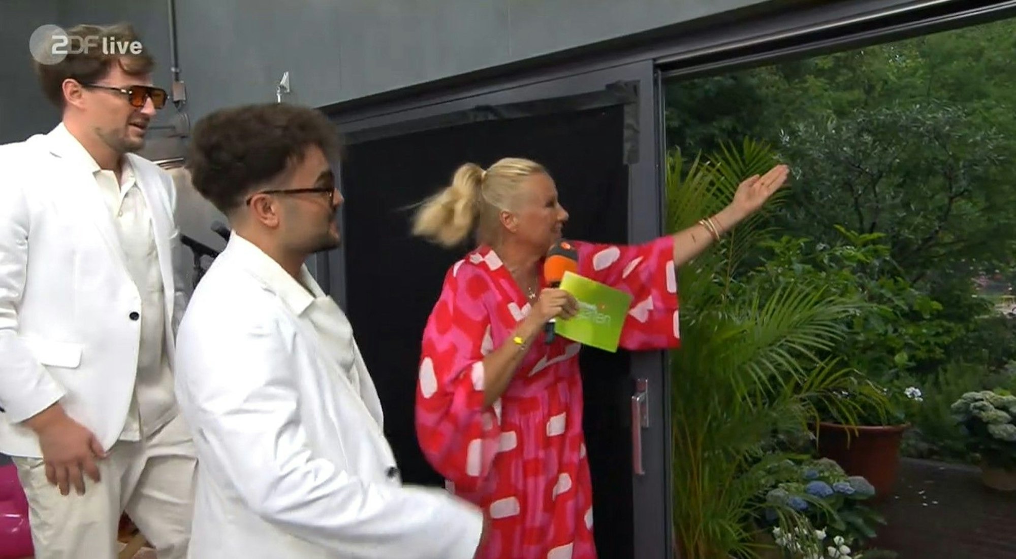 Schaut euch das an! Andrea Kiewel zeigt „Malle Anja“ den prasselnden Regen. Der ZDF-„Fernsehgarten“ musste kurzfristig aus dem Studio gesendet werden.