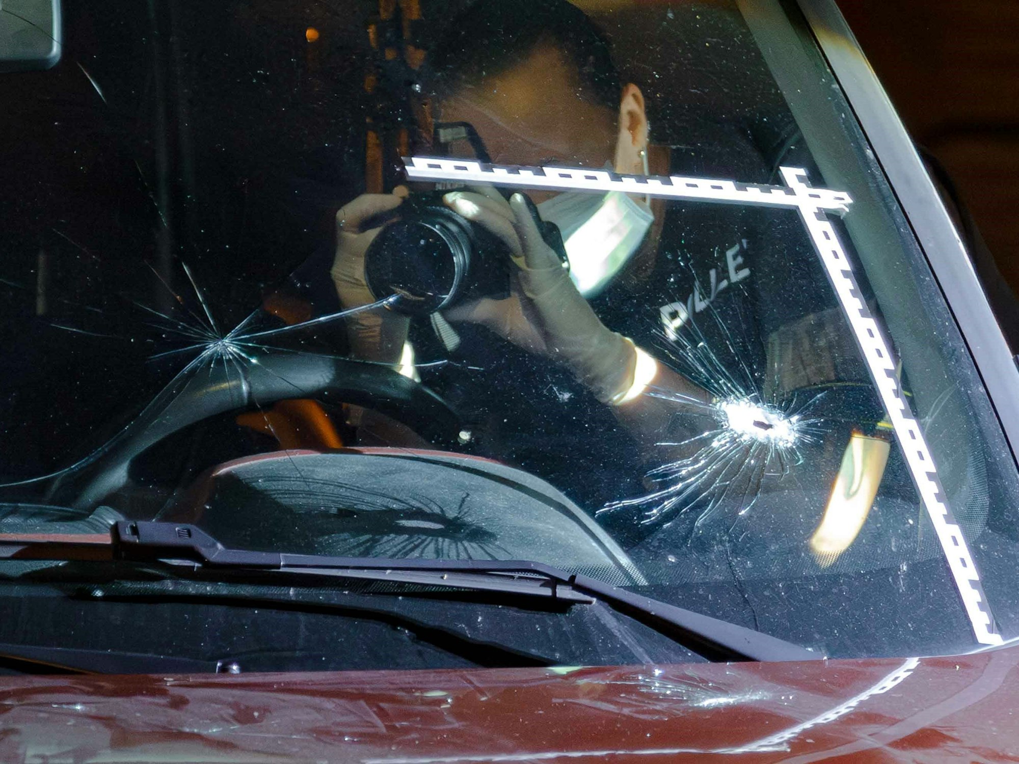 Ein Polizist fotografiert Einschusslöcher in einer Windschutzscheibe