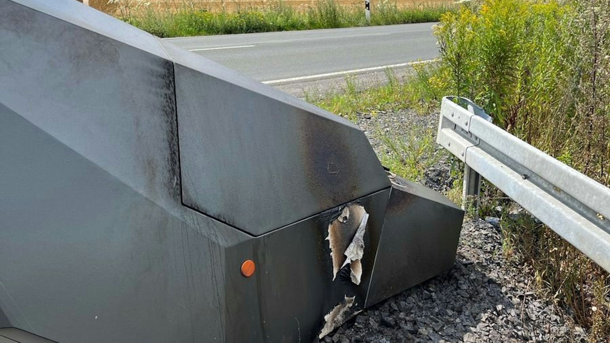 Ein ausgebrannter Blitzer-Anhänger steht am Straßenrand.
