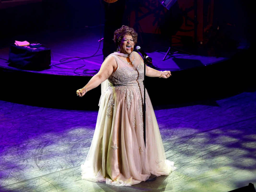 Eine Sängerin in einem strassbesetzten Tüllkleid steht im Scheinwerferlicht und singt.