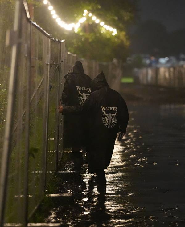 Metal-Fans gehen in der Nacht über einen überfluteten Weg auf dem Festivalgelände des Wacken Open Air (WOA).