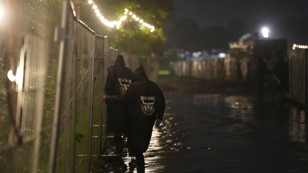 Metal-Fans gehen in der Nacht über einen überfluteten Weg auf dem Festivalgelände des Wacken Open Air (WOA).