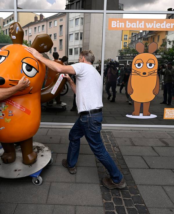 Zwei Männer schieben eine Maus-Figur auf einem Rollbrett weg.