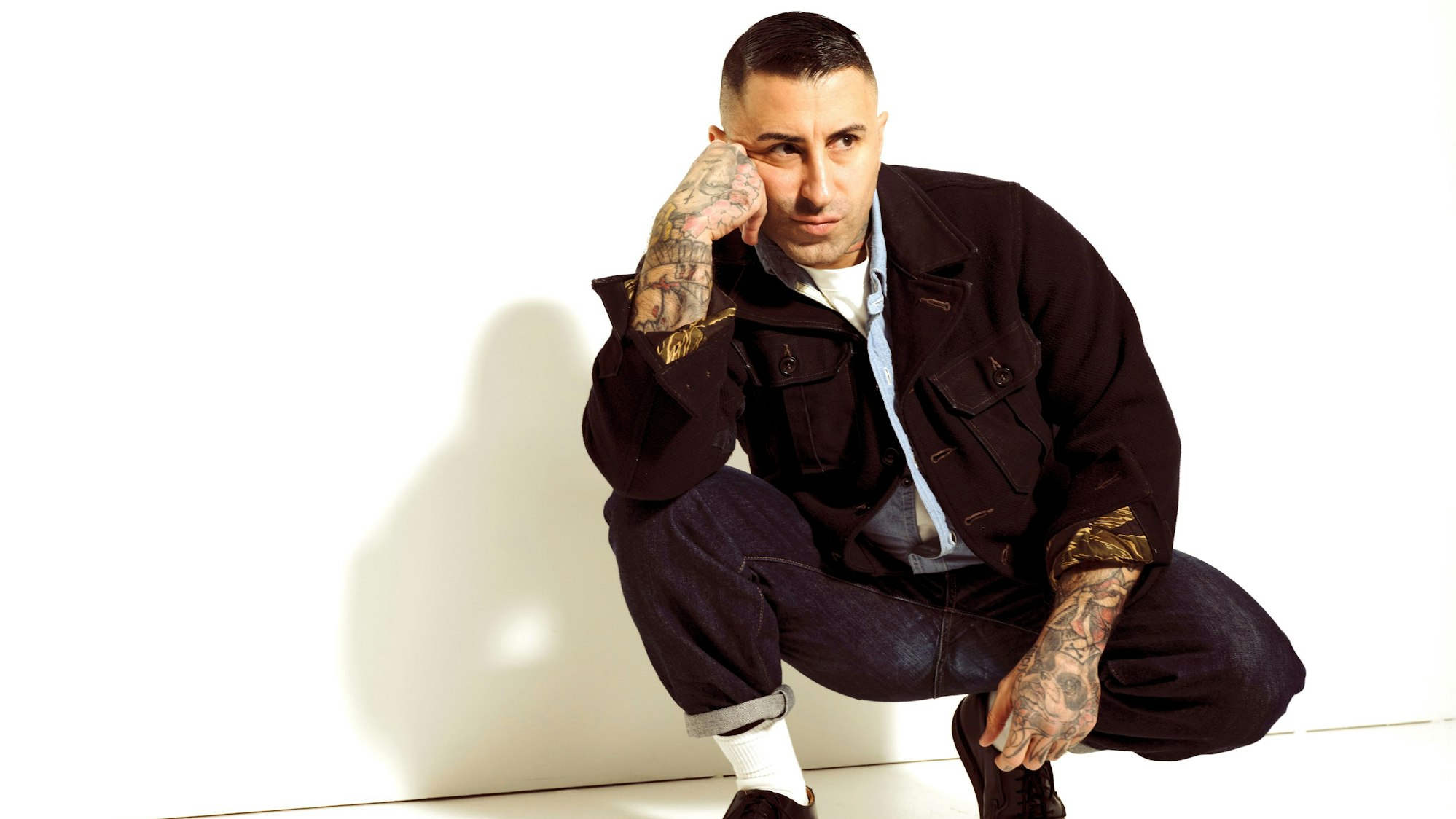 Ein Mann mit tätowierten Armen und schwarzem Outfit blickt nachdenklich