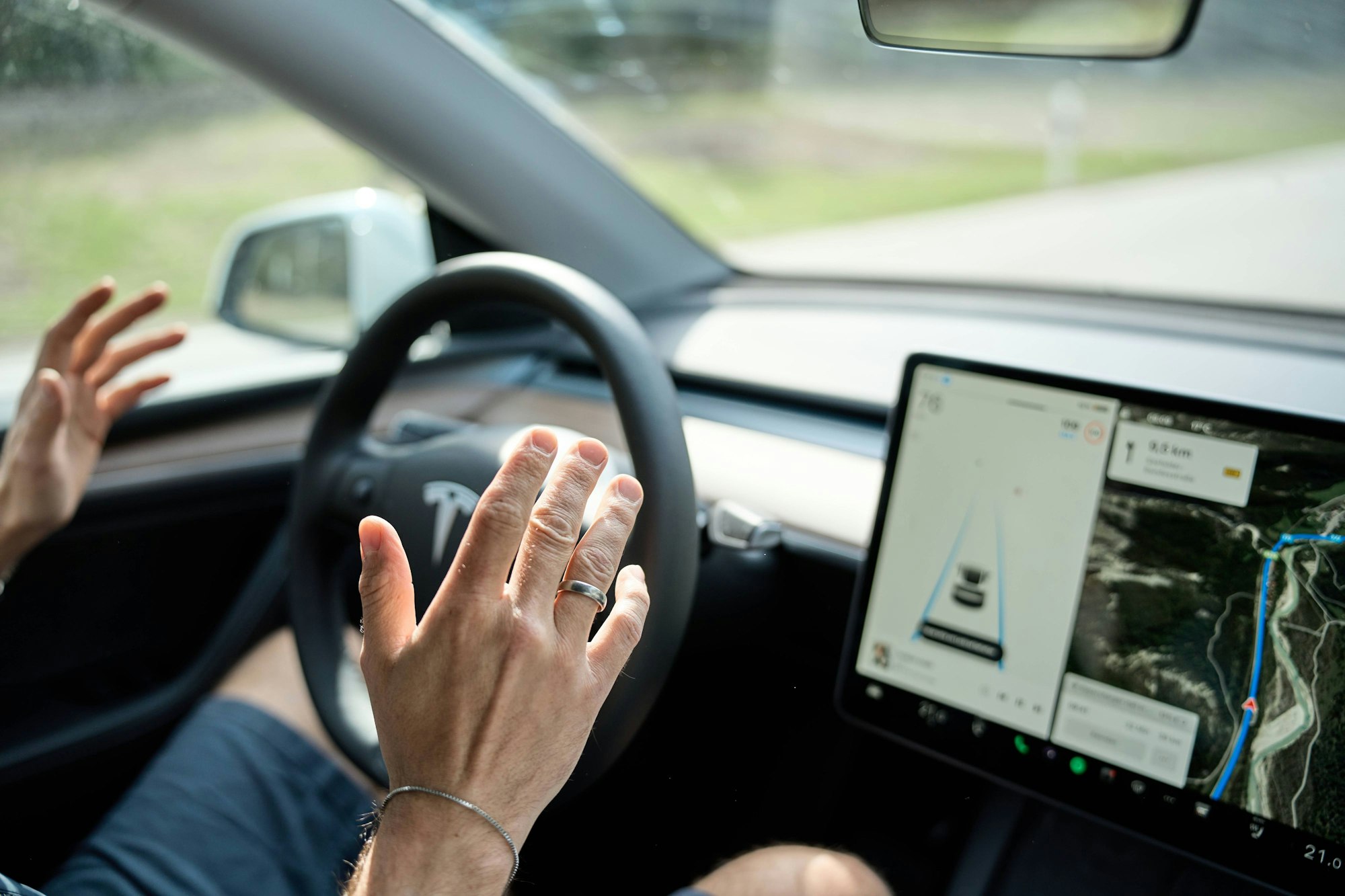 Ein Mann fährt mit einem Tesla E-Auto mit Autopilot. Er hält die Hände weg vom Lenkrad.