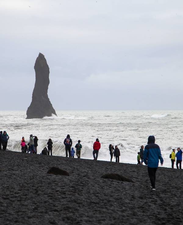 Touristen spazieren über den schwarzen Strand Reynisfjara.