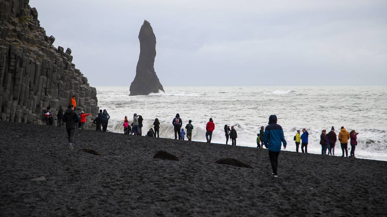 Touristen spazieren über den schwarzen Strand Reynisfjara.