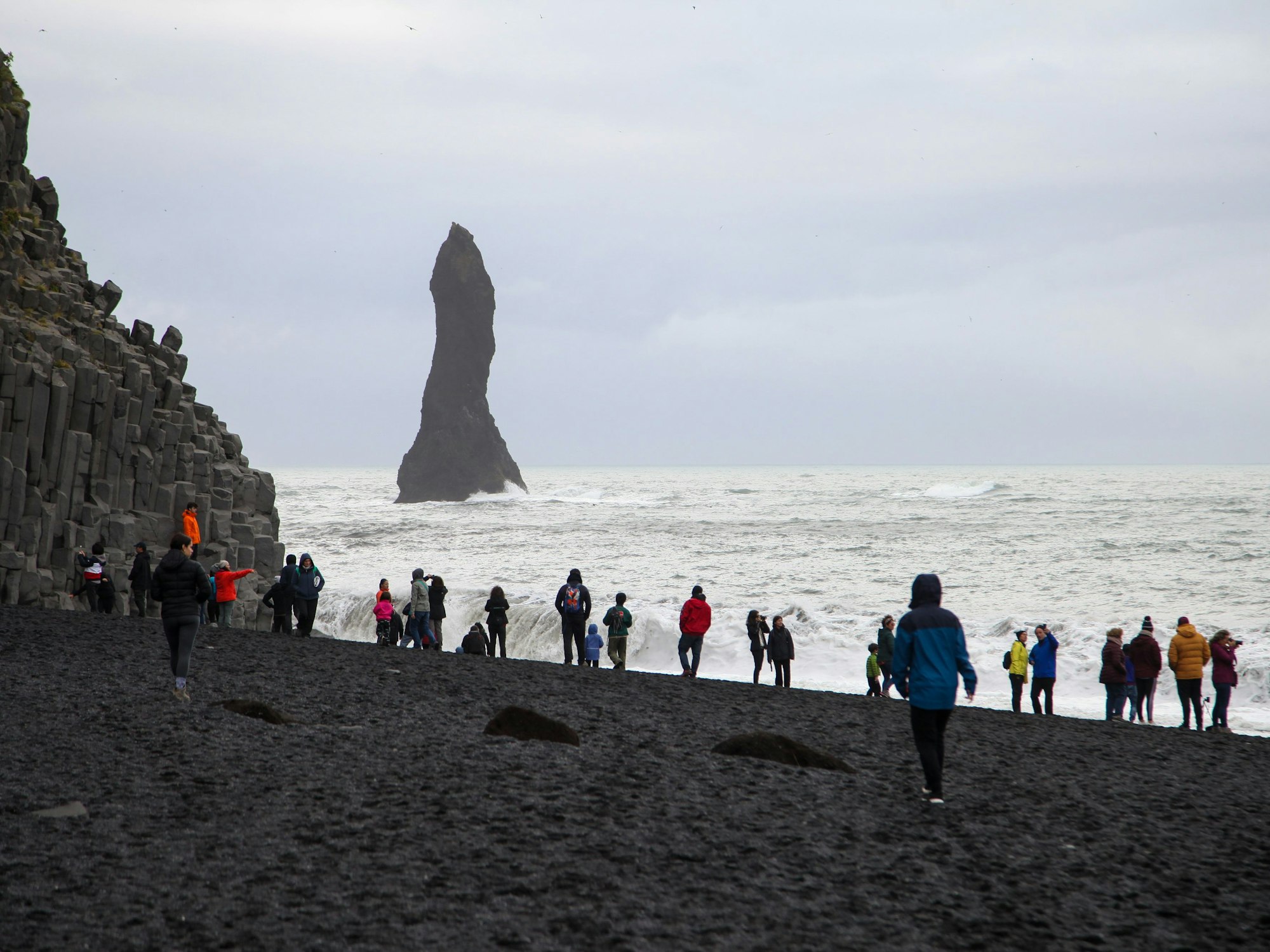 Touristen spazieren über den schwarzen Strand Reynisfjara.
