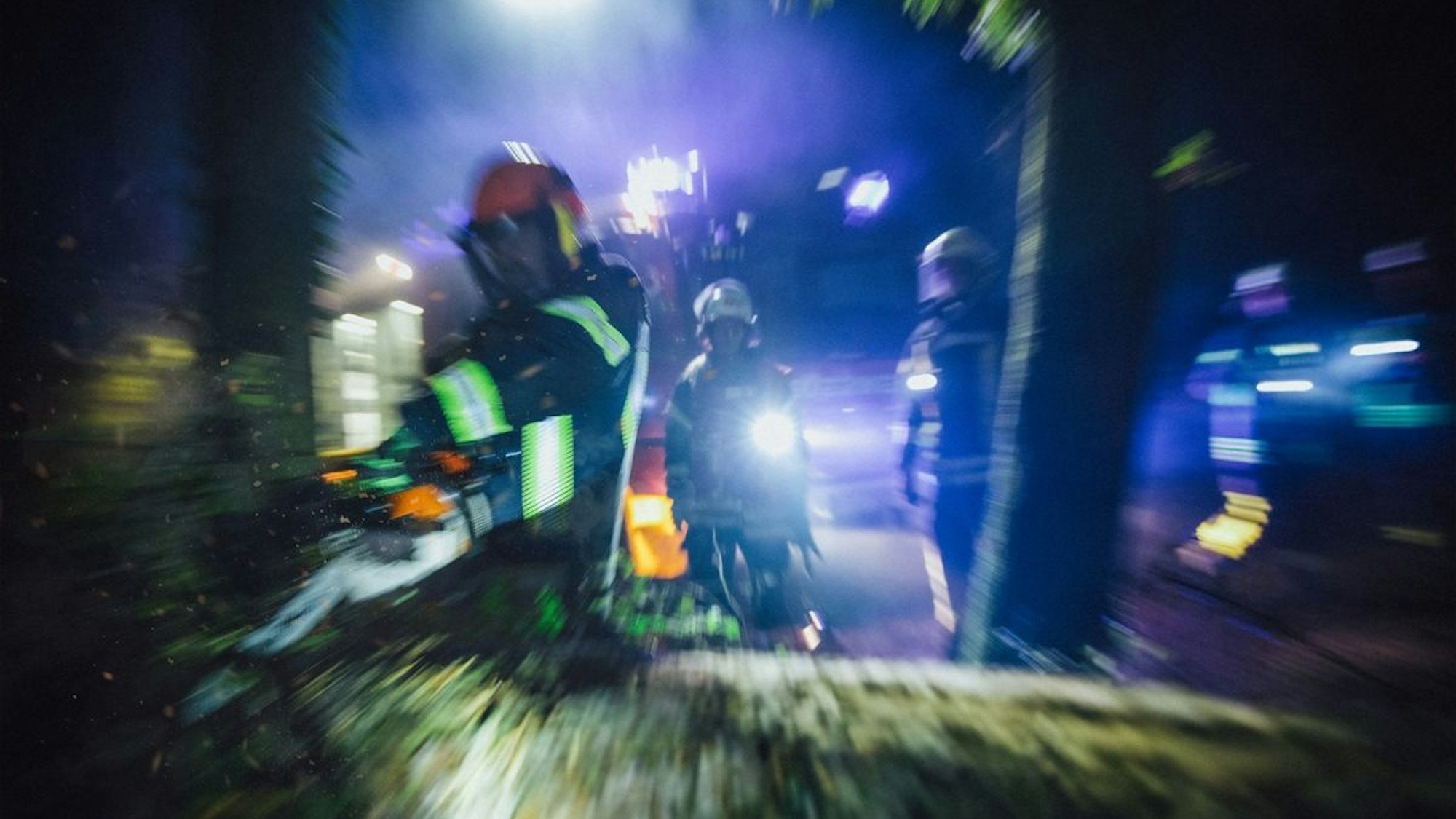 Ein großer Baum liegt quer über einer Straße und wird von der Feuerwehr zersägt.