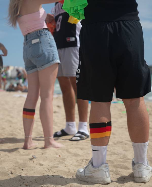 ARCHIV - 27.07.2025, Spanien, Palma: Menschen am Strand von Arenal in Mallorca tragen an ihren Waden Binden in den deutschen Farben. (zu dpa: «Ballermann im Theater: Duisburg bekommt Mallorca-Musical») Foto: Clara Margais/dpa +++ dpa-Bildfunk +++