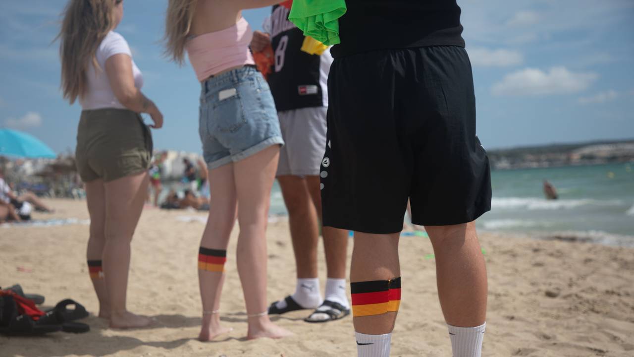 ARCHIV - 27.07.2025, Spanien, Palma: Menschen am Strand von Arenal in Mallorca tragen an ihren Waden Binden in den deutschen Farben. (zu dpa: «Ballermann im Theater: Duisburg bekommt Mallorca-Musical») Foto: Clara Margais/dpa +++ dpa-Bildfunk +++