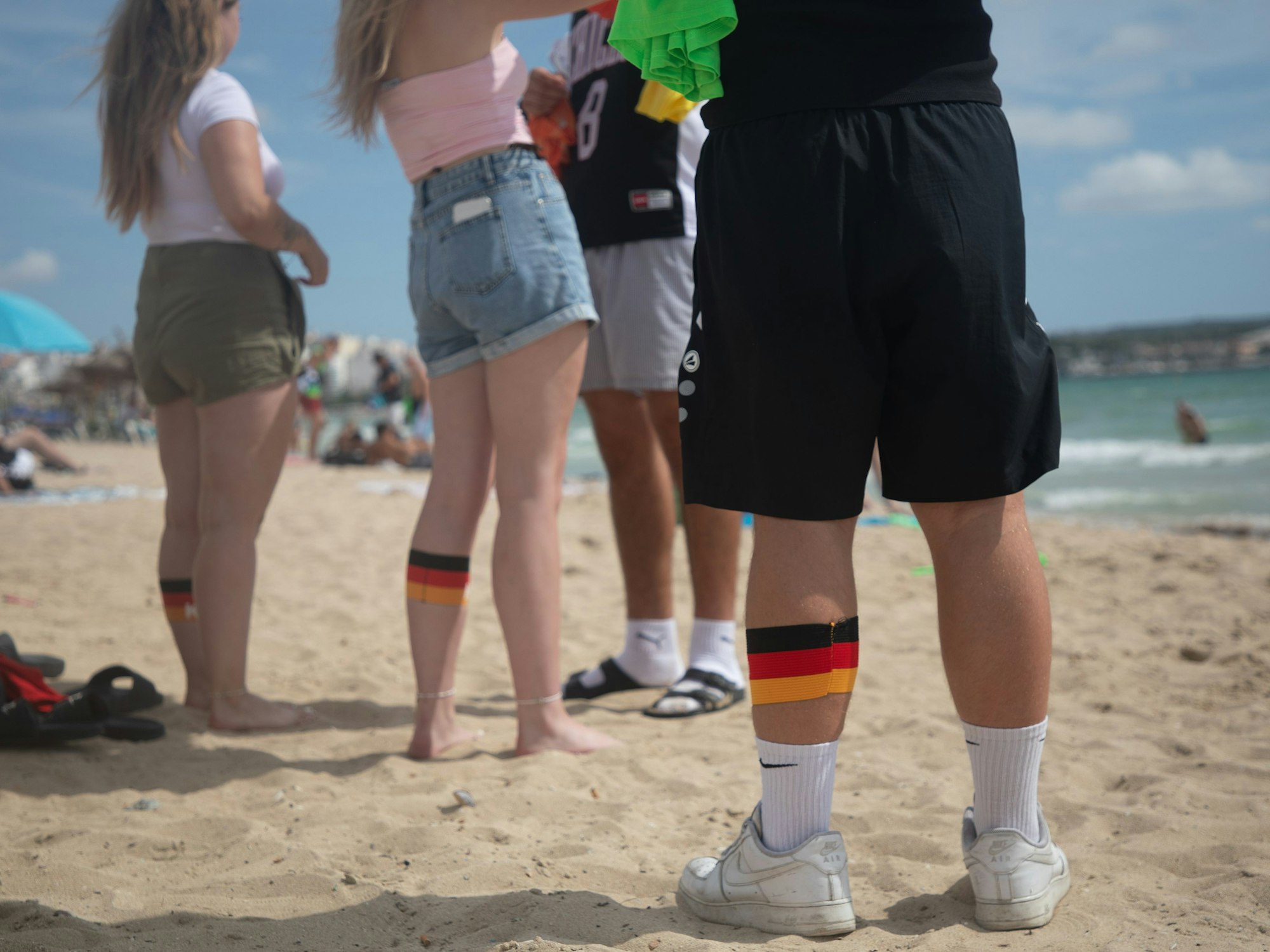 ARCHIV - 27.07.2025, Spanien, Palma: Menschen am Strand von Arenal in Mallorca tragen an ihren Waden Binden in den deutschen Farben. (zu dpa: «Ballermann im Theater: Duisburg bekommt Mallorca-Musical») Foto: Clara Margais/dpa +++ dpa-Bildfunk +++