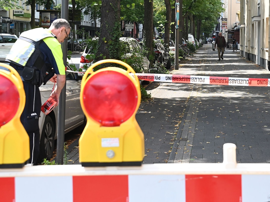 Ein Polizist sperrt einen Fußweg mit Flatterband ab.